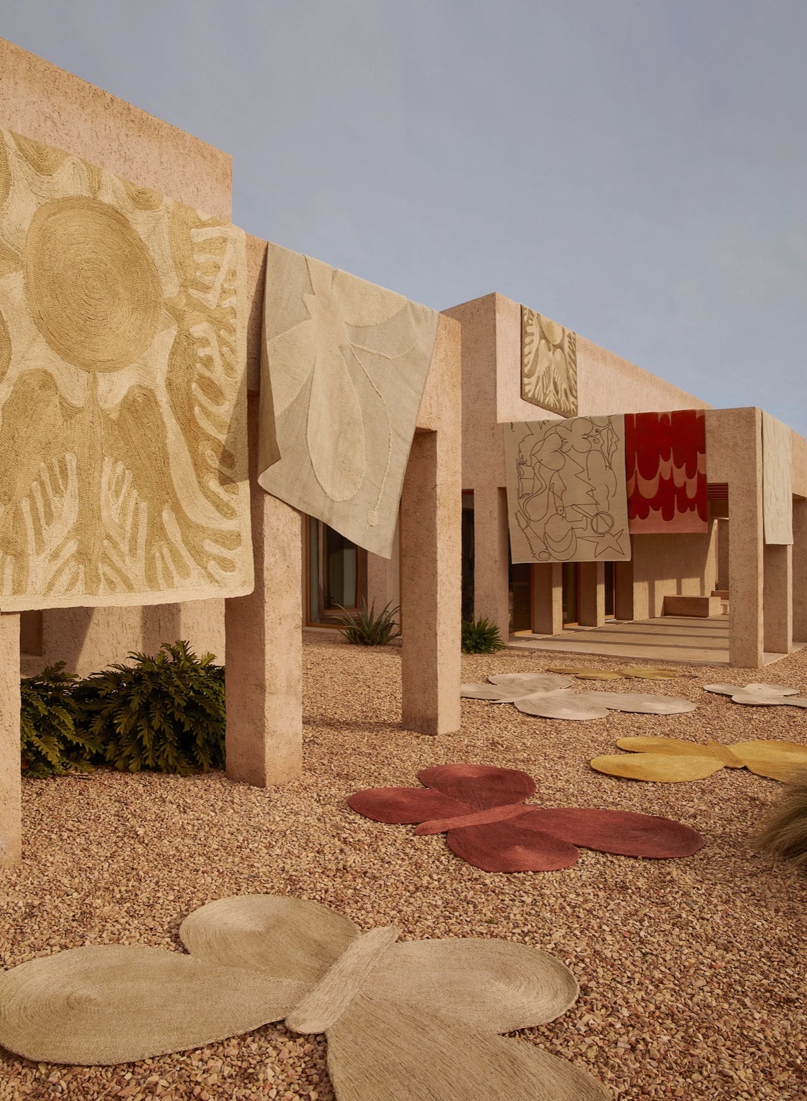 Lucia Eames Collection rugs by nanimarquina, shown outdoors against adobe walls, in sun, butterfly and bird motifs