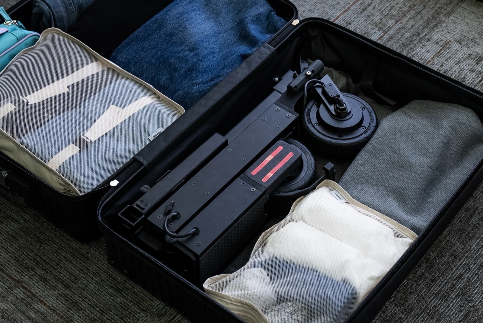 The folded Blizwheel F0.5 packed inside a suitcase alongside clothing and packing cubes, taking up a single narrow strip of space