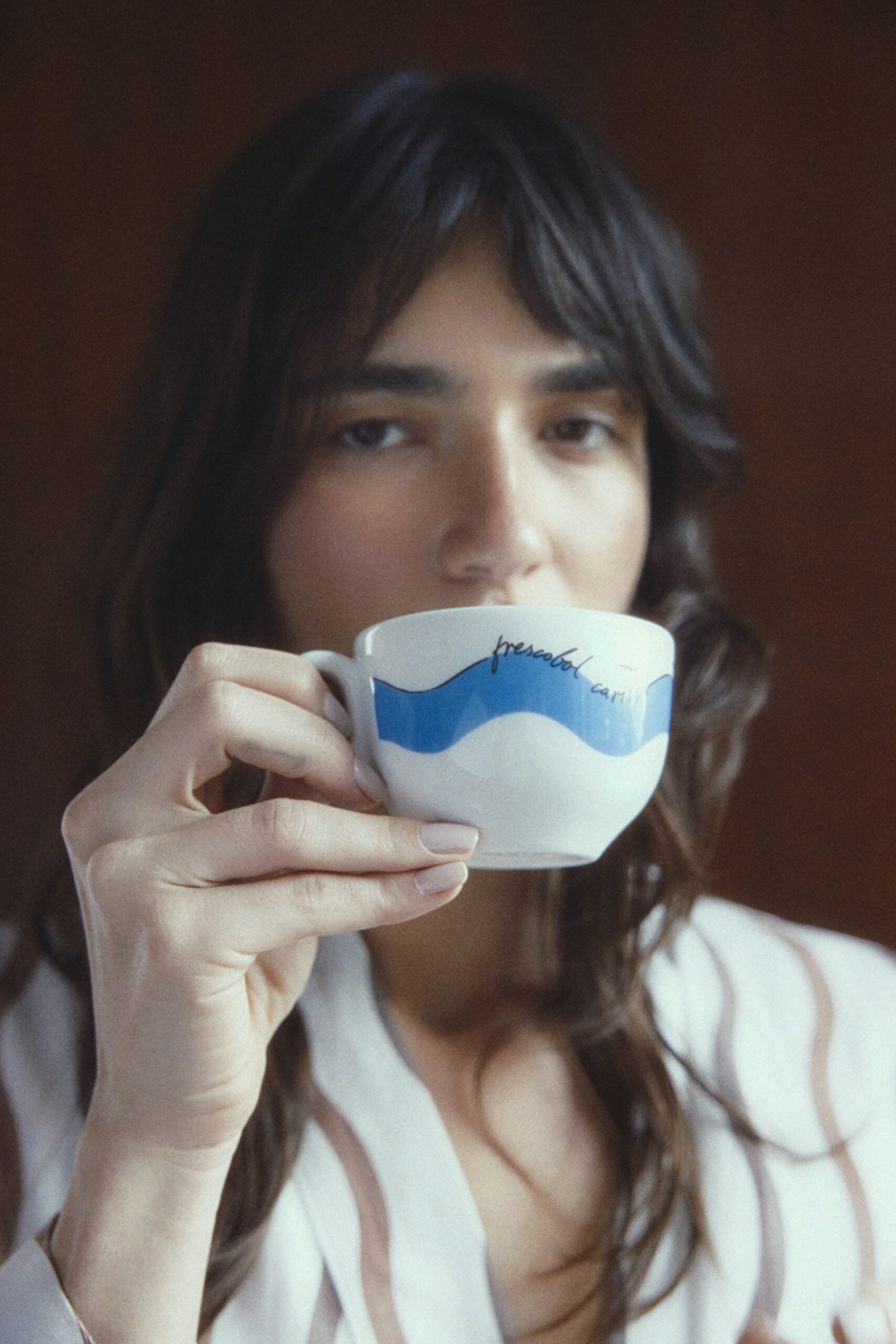 A model in a striped linen robe from the Cafezinho Carioca capsule collection, drinking from a Frescobol Carioca-branded La Marzocco mug