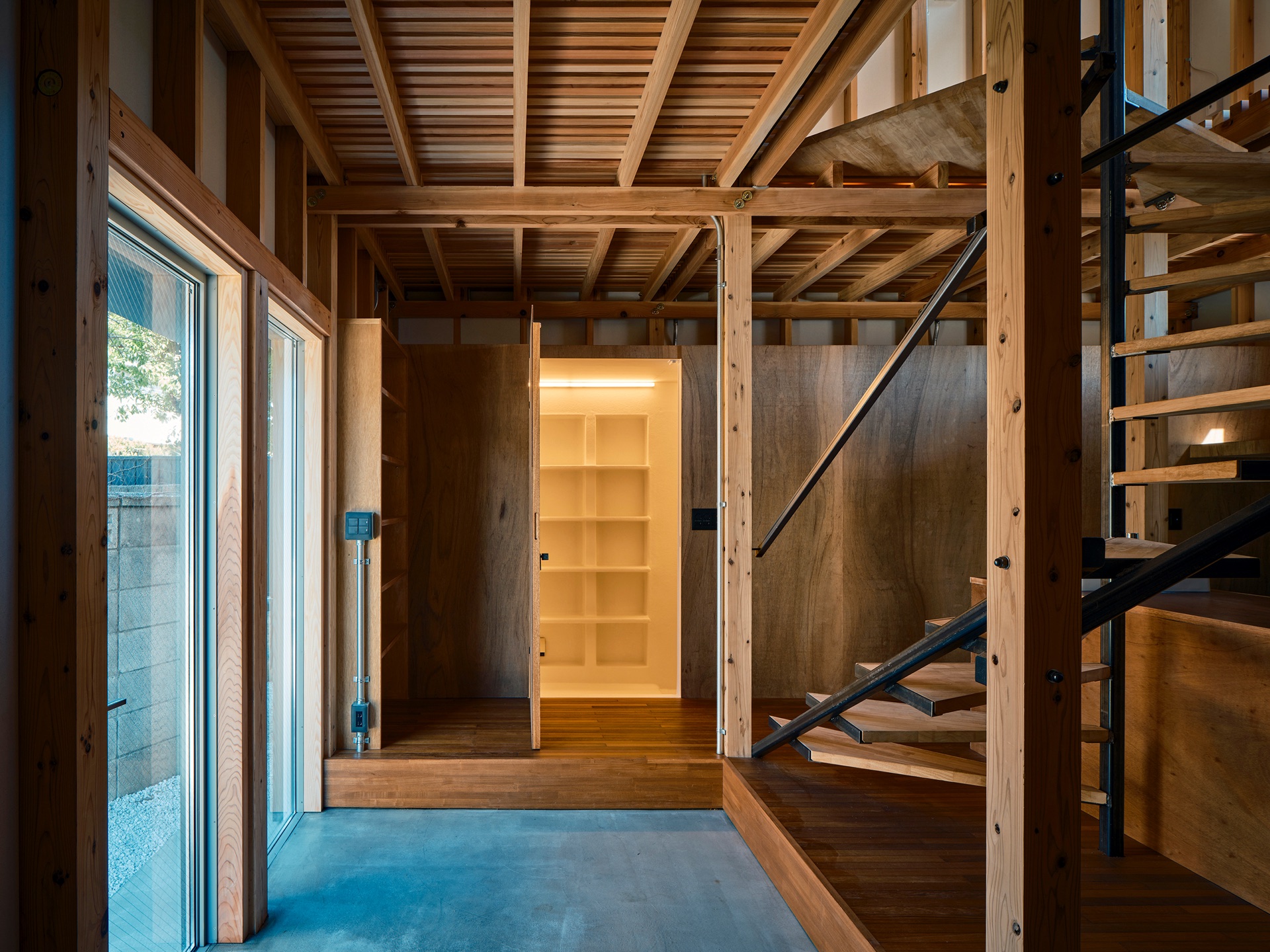 Interior view of Circularity House showing exposed timber posts, beams, and bolted joinery around an entryway, with a wood-slat staircase visible beyond
