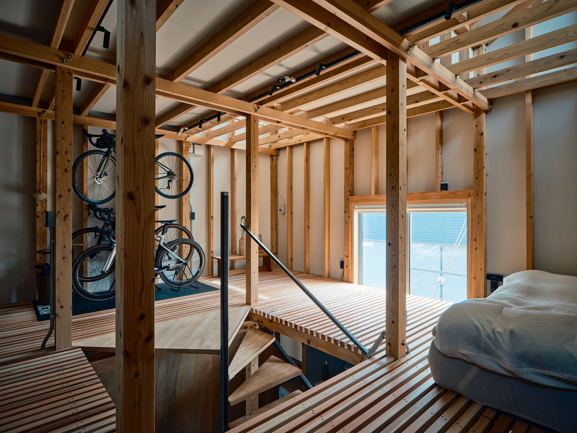A slatted wood floor and staircase inside Circularity House, with daylight from a large window casting long shadow lines across the slats